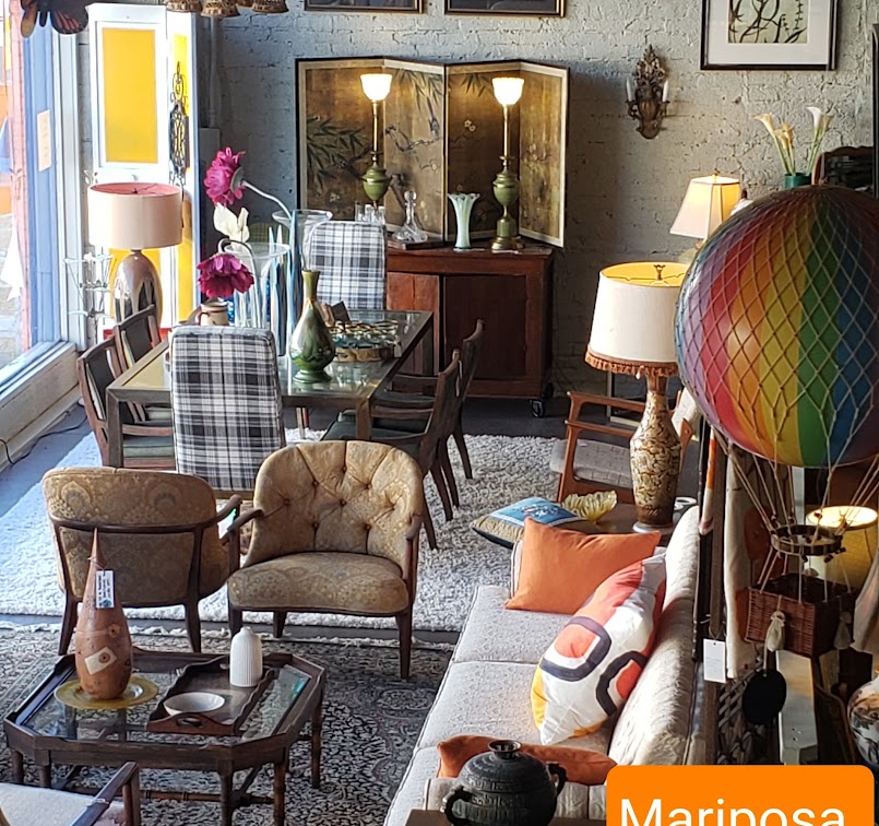 Mariposa, 805 Hobson Ave., Hot Springs, AR  71913 view of front riser in showroom from above. Includes a white brocade vintage sofa, curved back tan upholstered vintage armchairs, blue and white plaid parson's chairs, and other various decor and furniture.